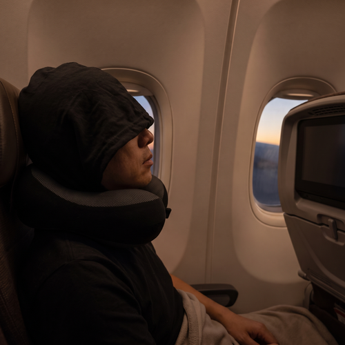 Passageiro a dormir no avião com a almofada de pescoço com capuz